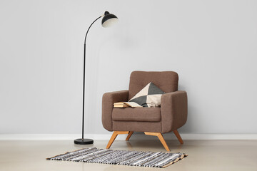 Cozy armchair with cushion and standard lamp near white wall