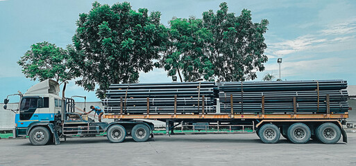 Trucks with long trailers carrying steel bars for building construction. Construction steel is...