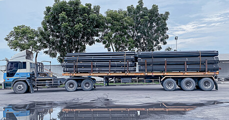 Trucks with long trailers carrying steel bars for building construction. Construction steel is...