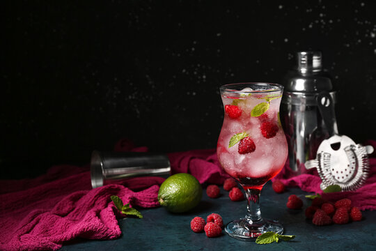 Glass of fresh raspberry mojito and shaker on blue table