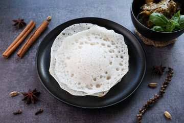 Appam, Kerala breakfast food duck curry or hot and spicy chickpea Masala and milk tea chai, Christian breakfast on dark black background. fermented rice pan cake. Top view of Indian veg food.