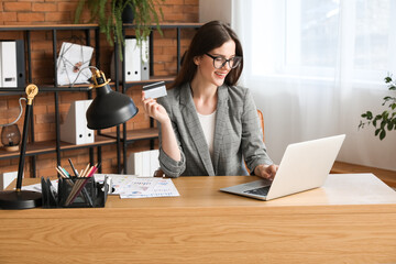 Young businesswoman with credit card using laptop at table in office