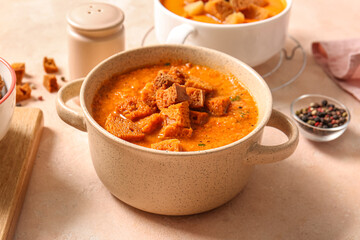 Pot of tasty cream soup with croutons on beige background