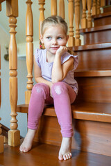 Little girl is sitting alone on stairs at home. Dangerous situation at home. Child safety concept. 