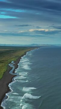 Aerial view of estuary on Khalaktyrsky beach with black sand and volcano on Kamchatka peninsula, Russia, Pacific ocean. Vertical video