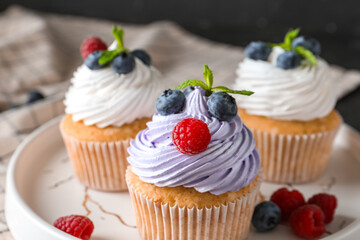 Plate of delicious cupcakes with blueberries, raspberries and mint on black background