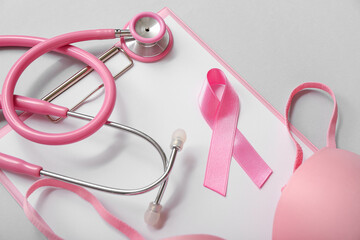 Pink ribbon with stethoscope, bra and clipboard on grey background. Breast cancer awareness concept