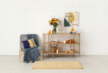 Shelving unit with bouquet of autumn flowers and armchair near white brick wall