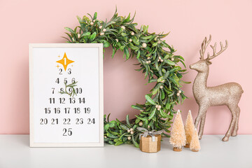Christmas calendar with wreath and decor on shelf near pink wall
