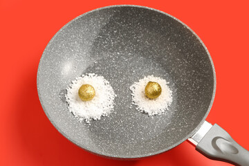 Frying pan with eggs made of snow and Christmas balls on red background