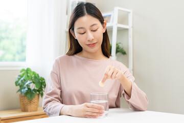 Smile asian young woman putting or dropping effervescent tablet into glass of water, holding pain pill, painkiller medicine, aspirin for treatment, take vitamin c for hangover. Health care concept.