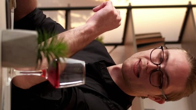 Vertical video. Work toast. Freelancer lifestyle. Successful project. Relaxed business man taking break raising glass drinking red wine alcohol at modern home workplace interior.