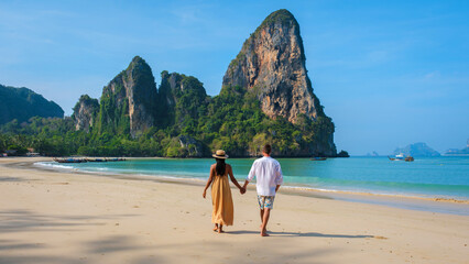 A couple of men and woman walking on the beach of Railay Beach Krabi Thailand on a early morning...
