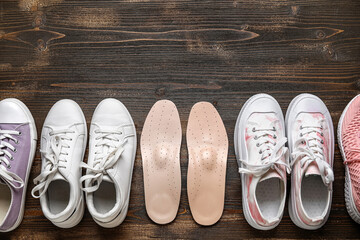 Set of different female shoes and orthopedic insoles on wooden background