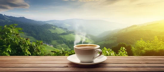 Rolgordijnen Coffee and tea cups steaming on a wooden table surrounded by a mountainous city landscape with sunlit beauty and blurred green bokeh background Lifestyle concept © Vusal