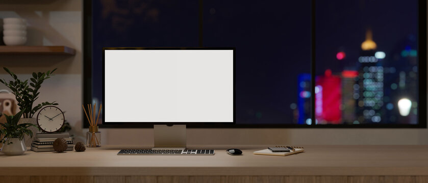 A computer monitor mockup on a wooden desk against the window with a city night light view.
