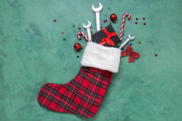 Composition with Christmas sock, gift box and wrenches on green background