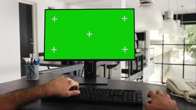 POV of businessman works at greenscreen pc in front of computer, solving daily tasks and looking at monitor running blank chromakey template at workstation. Worker uses mockup screen. Tripod shot.