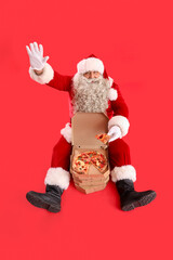 Santa Claus with tasty pizza sitting on red background