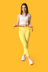 Beautiful young sporty woman with measuring tape on yellow background. Weight loss concept