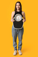 Beautiful young sporty woman with scales on yellow background. Weight loss concept