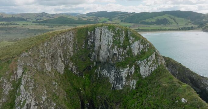 Aerial drone flying over steep rocky cape landscape towards beautiful peaceful sandy beach in remote Cannibal Bay in the Catlins, South Island of New Zealand Aotearoa