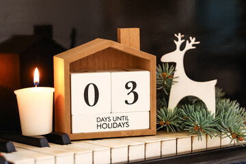 Calendar with text 3 DAYS UNTIL HOLIDAYS, burning candle and Christmas decorations on piano keys, closeup