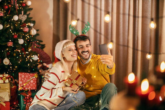 A happy couple sitting at home on christmas and new year's eve and taking selfies with christmas gift.