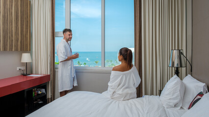 a couple on vacation drinking coffee in the morning looking out the window over the beach and ocean during a luxury holiday