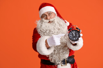 Santa Claus pointing at alarm clock on orange background