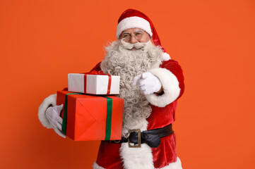 Santa Claus with Christmas gifts pointing at viewer on orange background