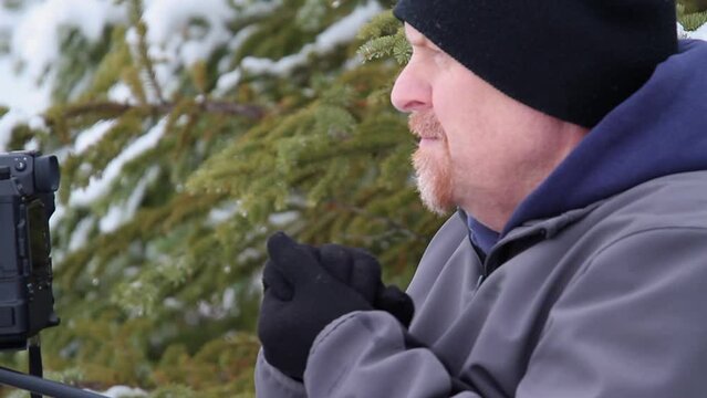 Cold winter male photographer in conifer forest warms gloved hands