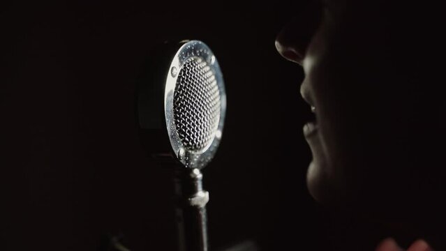Woman aggressively speaking propoganda into a vintage microphone in a close up shot in a dark room. Delivering audio information and radio broadcasting.