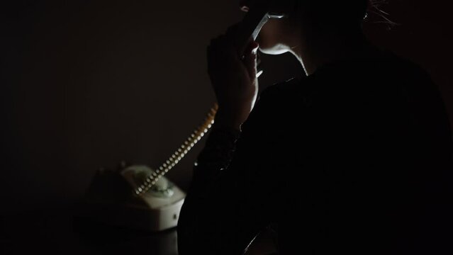 Waiting for an Important Call. Late night gossip on the vintage landline telephone, shot from the back. Retro vibes interior desk scene with a woman talking on the phone in low light.