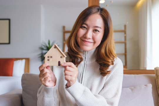 Portrait image of a young woman holding and showing a wooden house model