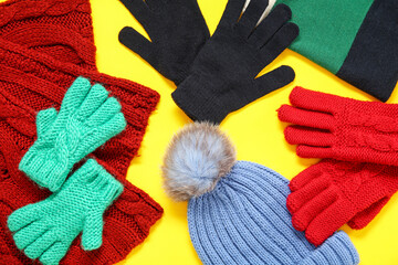 Composition with different warm gloves, hats and scarf on yellow background