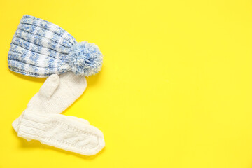 Stylish knitted hat and mittens on yellow background