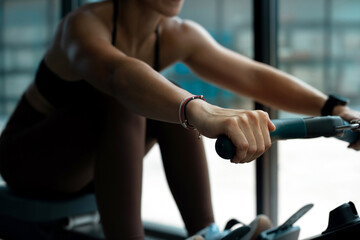 Fitness girl workout on indoor rower at the gym, doing exercises on rowing machine near the window,...