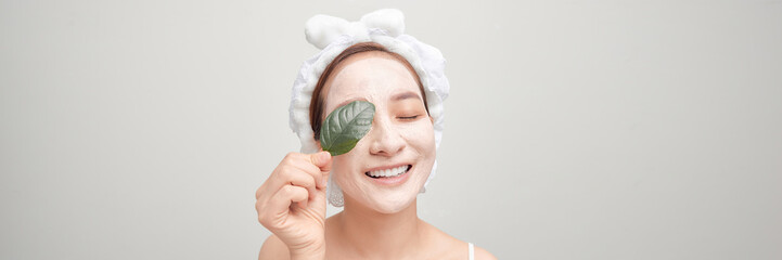 Woman with a clay mask on her face holds a green leaf. Panorama