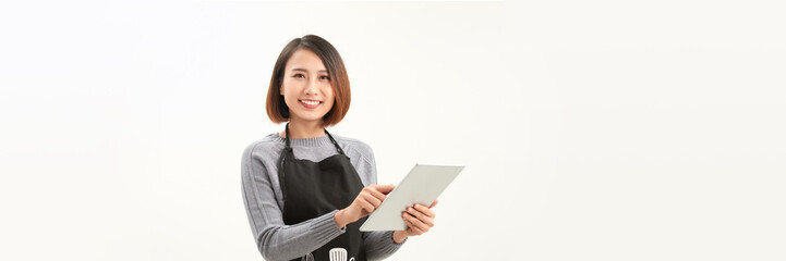 Friendly cute female barista in black apron smiling at camera, using digital tablet to manage cafe orders