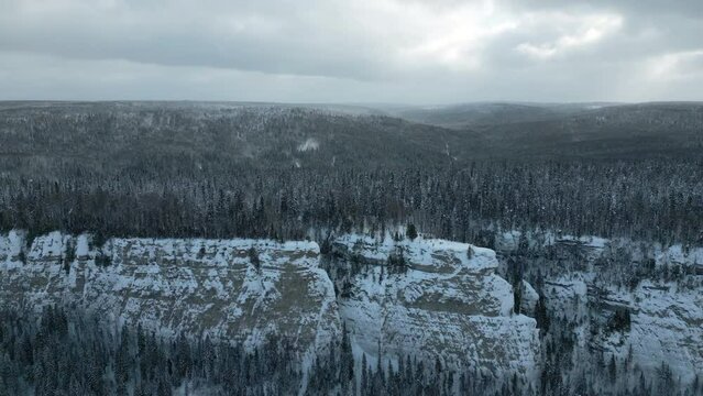 Aerial view of mountain cliff and river. Clip. Frosty cold snowy morning and the endless evergreen pine forest.