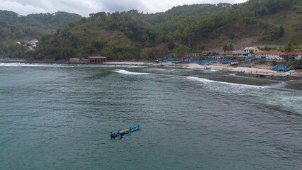Obraz premium Drone view of Menganti Beach with white sand, calm waves, cliffs and green trees and the activities of traditional fishermen and traditional fishing boats