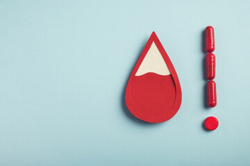 Red blood drop and exclamation point made from pills on pastel blue background. Iron deficiency anemia, hemophilia, blood donation concept. Top view, copy space