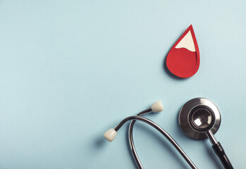 Red blood drop with medical stethoscope on pastel blue background. Iron deficiency anemia,...