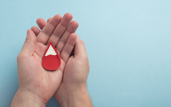 Man holding red blood drop on pastel blue background. Anemia, hemophilia, blood donation concept. Top view, copy space