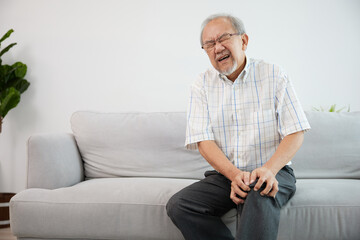 senior man suffering from knee ache on sofa