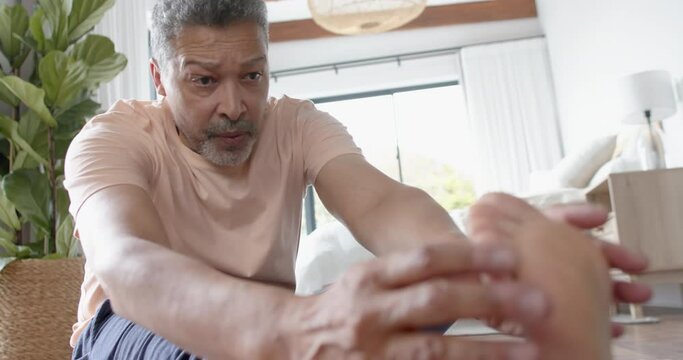 Focused senior biracial man practicing yoga, stretching at home, slow motion