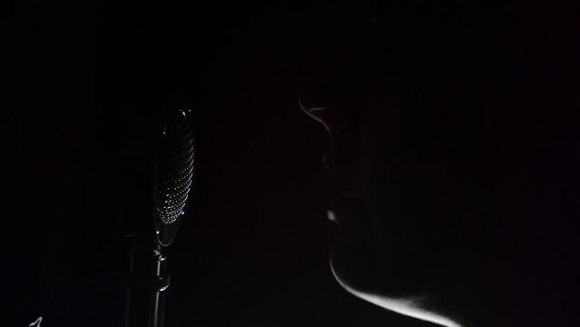 Podcaster Talking In A Microphone In Dark Studio. Close up footage of a woman speaking to a microphone.