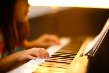 Close-up of a little student's hand playing the piano. Happy young Asian girl learning and...