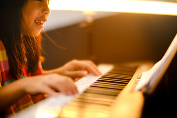 Close-up of a little student's hand playing the piano. Happy young Asian girl learning and...